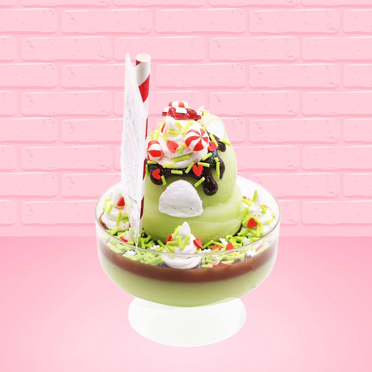 Cute kawaii ice cream Emotional Grinch Fudge sundae which has a sign and green white and red heart sprinkles inside of the dish as well as swirls of whipped cream. The bunny has chocolate glaze, peppermint candies and a swirl of whipped cream on it’s head. This view is from the back.