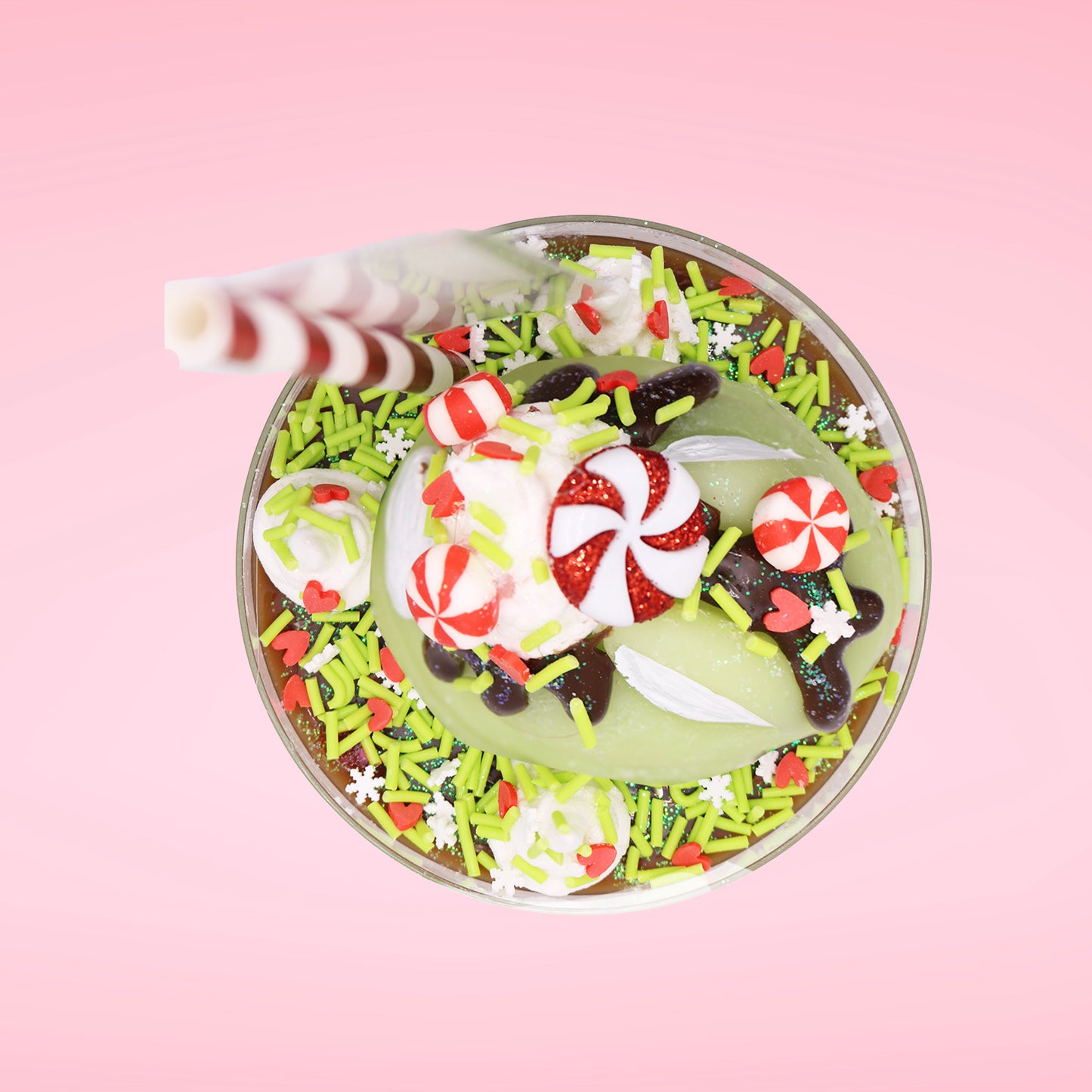 Cute kawaii ice cream Emotional Grinch Fudge sundae which has a sign and green white and red heart sprinkles inside of the dish as well as swirls of whipped cream. The bunny has chocolate glaze, peppermint candies and a swirl of whipped cream on it’s head. This view is from the top.