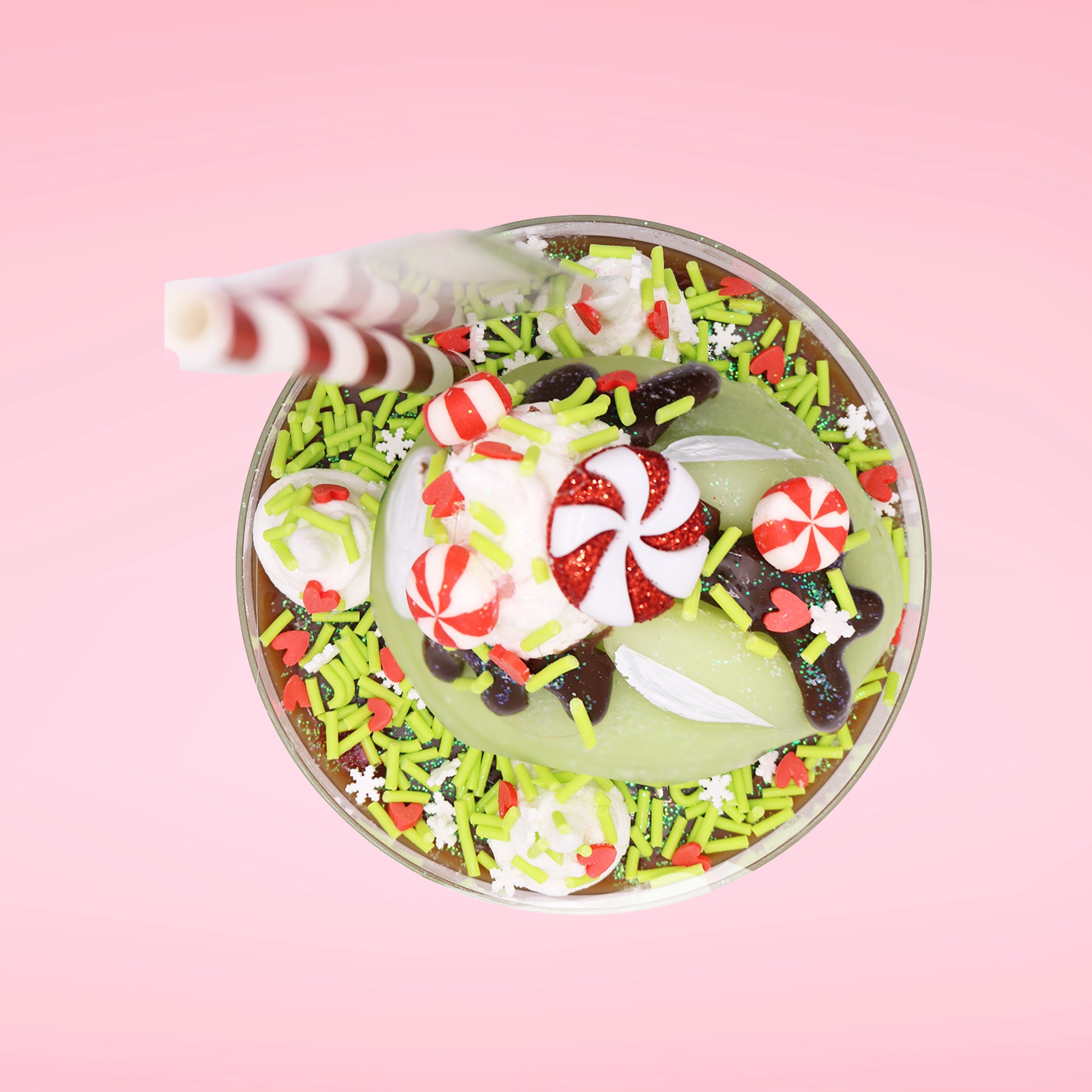 Cute kawaii ice cream Emotional Grinch Fudge sundae which has a sign and green white and red heart sprinkles inside of the dish as well as swirls of whipped cream. The bunny has chocolate glaze, peppermint candies and a swirl of whipped cream on it’s head. This view is from the top.