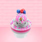 Cute kawaii unicorn bunny Irresistible Sugary Berry light blue and pink sundae with light blue and pink sprinkles with whipped cream swirls in the dish.  The unicorn bunny has blue berries and red raspberries on top near the whipped cream swirl with white drizzle coming down. This view is from the front.