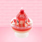 Cute kawaii bunny new strawberry cheesecake white ice cream with red translucent glaze, strawberries, and swirls of whipped cream in the dish. The bunny has red glittery glaze dripping over the head with a strawberry and a swirl of whipped cream on top. This view is from the front.