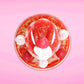 Cute kawaii bunny new strawberry cheesecake white ice cream with red translucent glaze, strawberries, and swirls of whipped cream in the dish. The bunny has red glittery glaze dripping over the head with a strawberry and a swirl of whipped cream on top. This view is from the top.