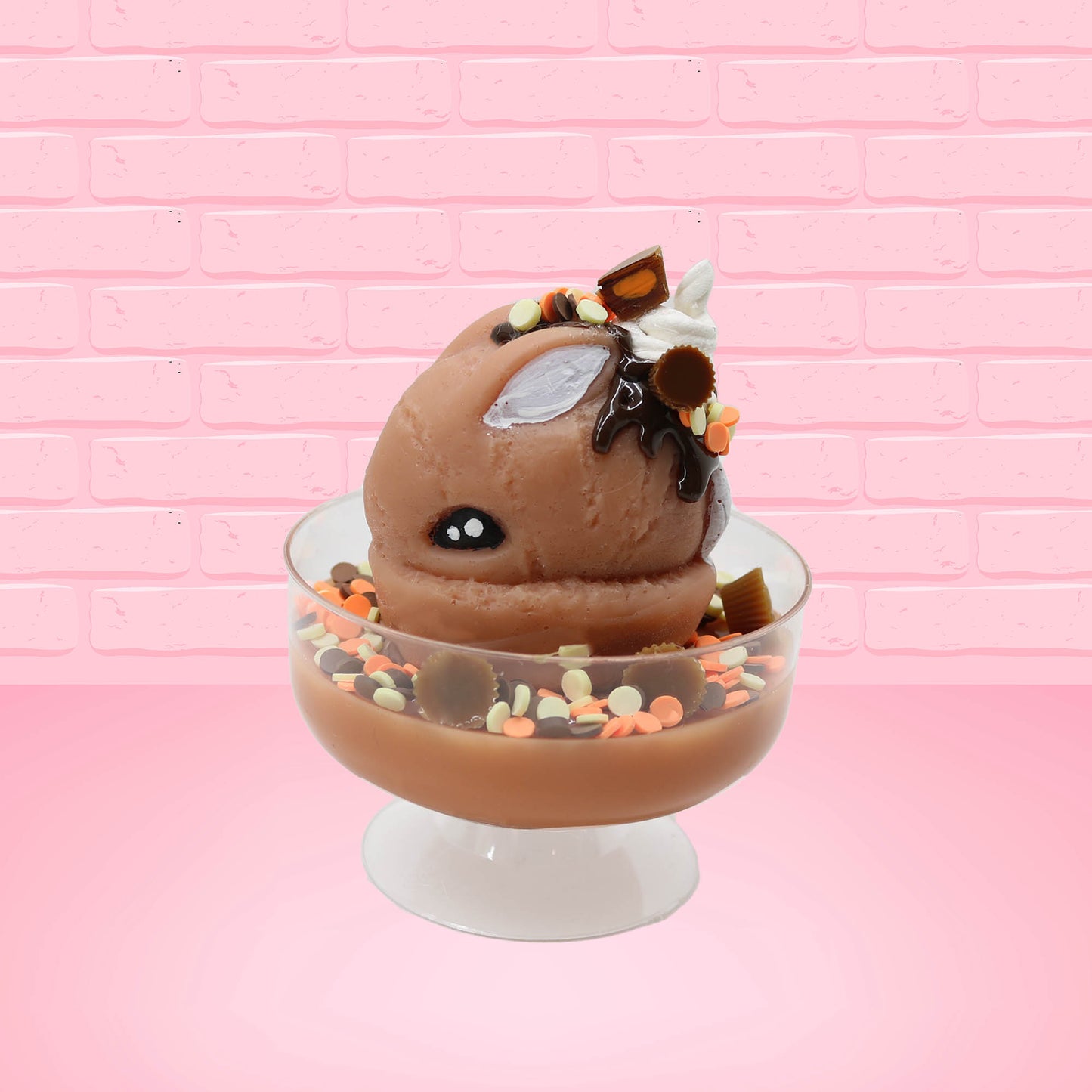 Cute kawaii peanut chocolate cup resin ice cream sundae with orange and white sprinkles in the dish. Chocolate drizzle and cups are on the top of the resin ice cream bunny, and a swirl whipped cream on top from the side.