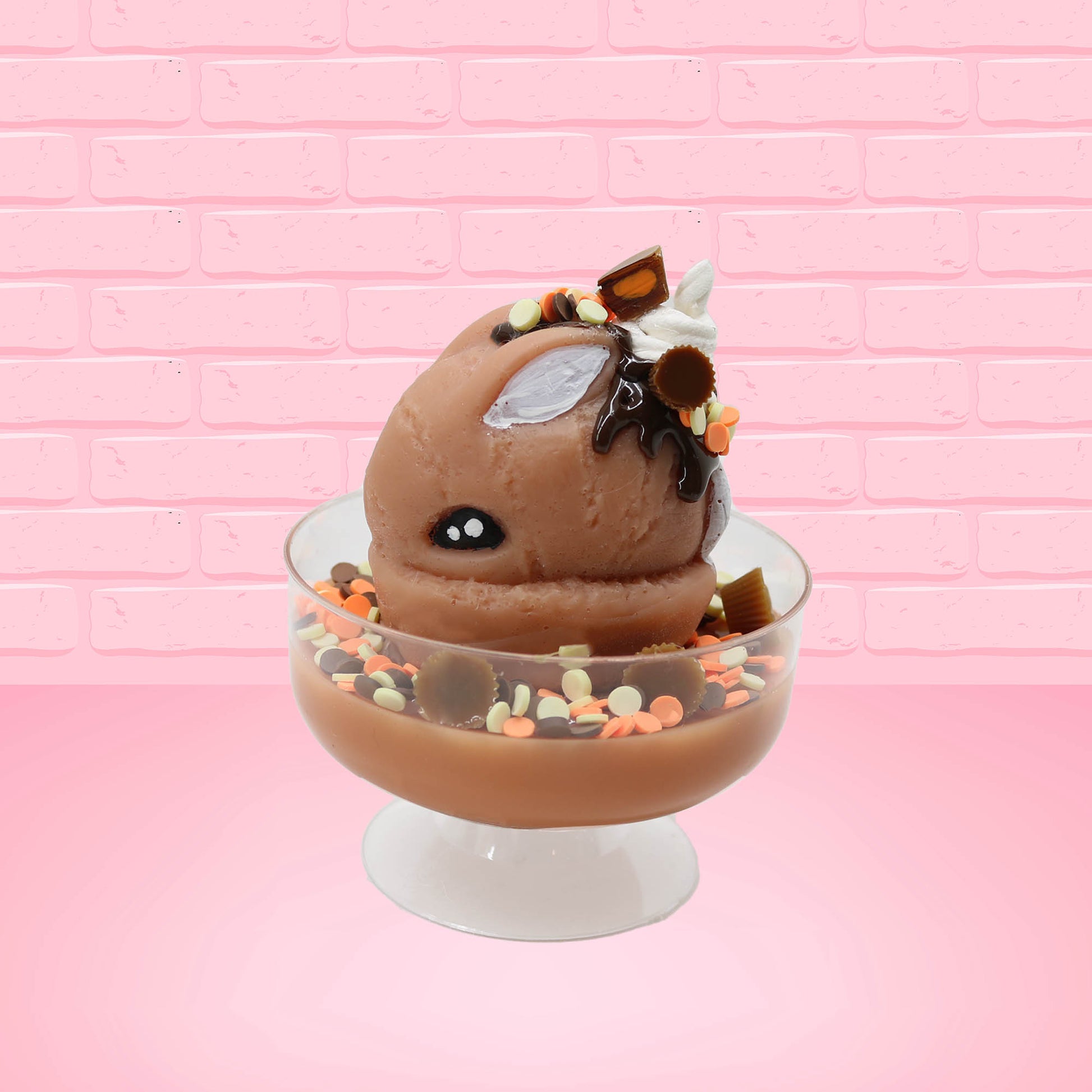 Cute kawaii peanut chocolate cup resin ice cream sundae with orange and white sprinkles in the dish. Chocolate drizzle and cups are on the top of the resin ice cream bunny, and a swirl whipped cream on top from the side.