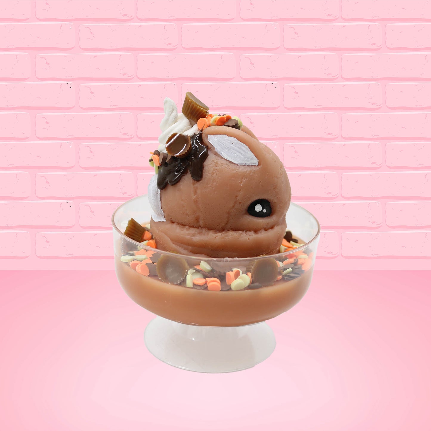 Cute kawaii peanut chocolate cup resin ice cream sundae with orange and white sprinkles in the dish. Chocolate drizzle and cups are on the top of the resin ice cream bunny, and a swirl whipped cream on top from the other side.