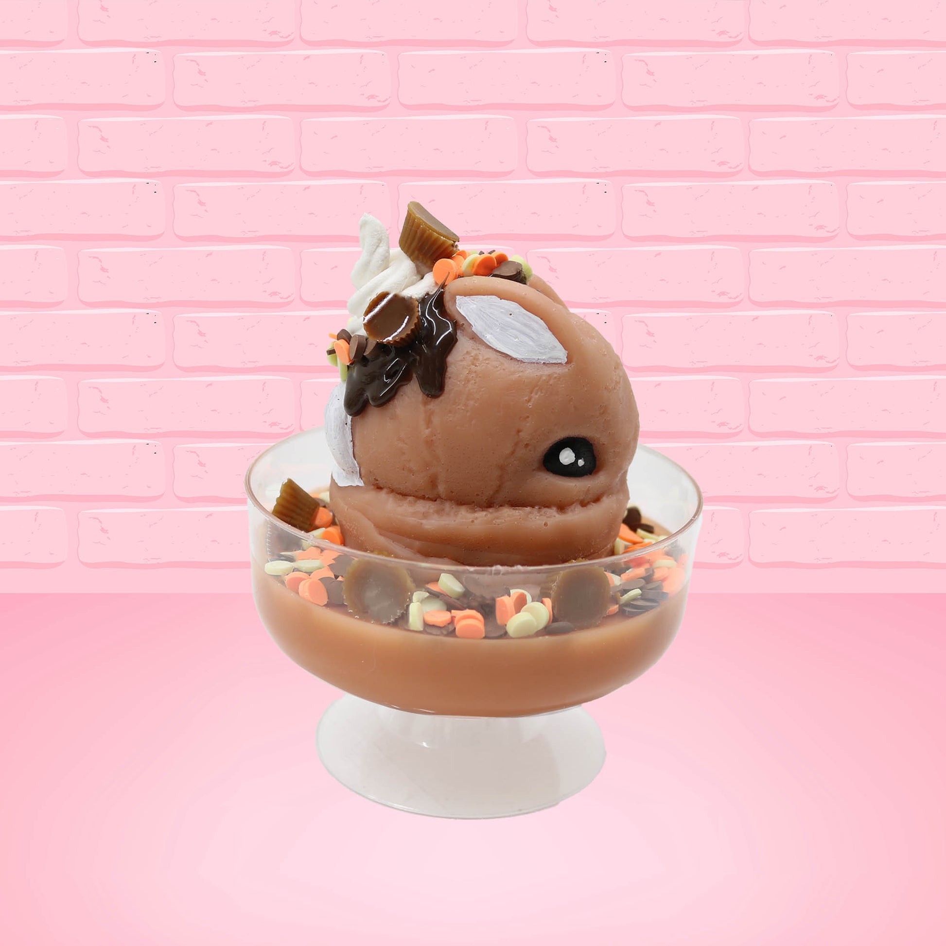 Cute kawaii peanut chocolate cup resin ice cream sundae with orange and white sprinkles in the dish. Chocolate drizzle and cups are on the top of the resin ice cream bunny, and a swirl whipped cream on top from the other side.