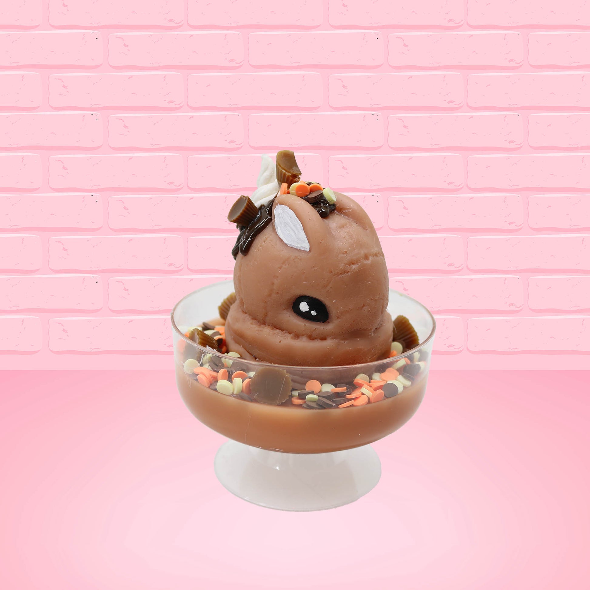 Cute kawaii peanut chocolate cup resin ice cream sundae with orange and white sprinkles in the dish. Chocolate drizzle and cups are on the top of the resin ice cream bunny, and a swirl whipped cream on top at a slight angle from the front.