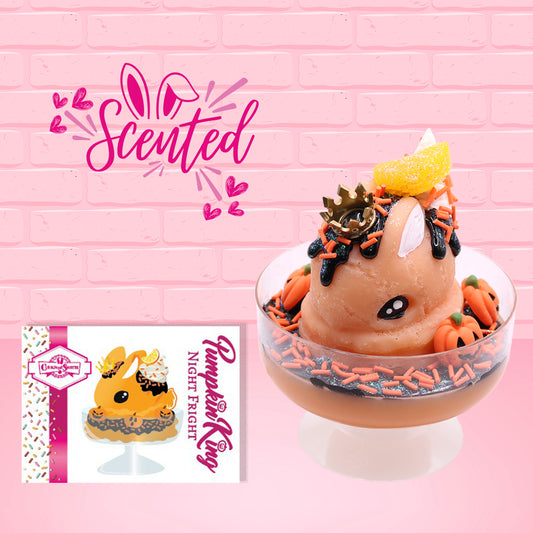 Cute kawaii Pumpkin King Bunny orange ice cream sundae with black glaze, orange sprinkles and pumpkin faces in the dish.  The bunny has a golden crown and orange slice on top next to the swirl of whipped cream. The character card front is shown as well as the word scented. 