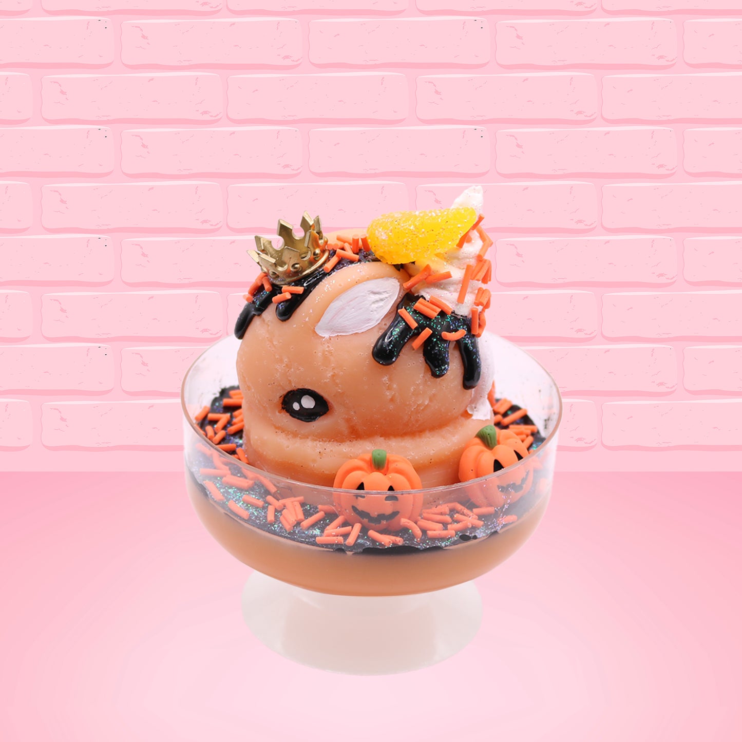Cute kawaii Pumpkin King Bunny orange ice cream sundae with black glaze, orange sprinkles and pumpkin faces in the dish.  The bunny has a golden crown and orange slice on top next to the swirl of whipped cream. This view is from the side.