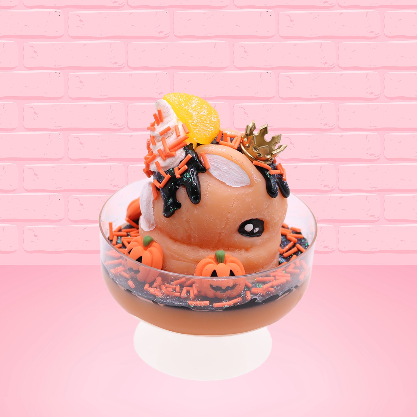 Cute kawaii Pumpkin King Bunny orange ice cream sundae with black glaze, orange sprinkles and pumpkin faces in the dish.  The bunny has a golden crown and orange slice on top next to the swirl of whipped cream. This view is from the other side.