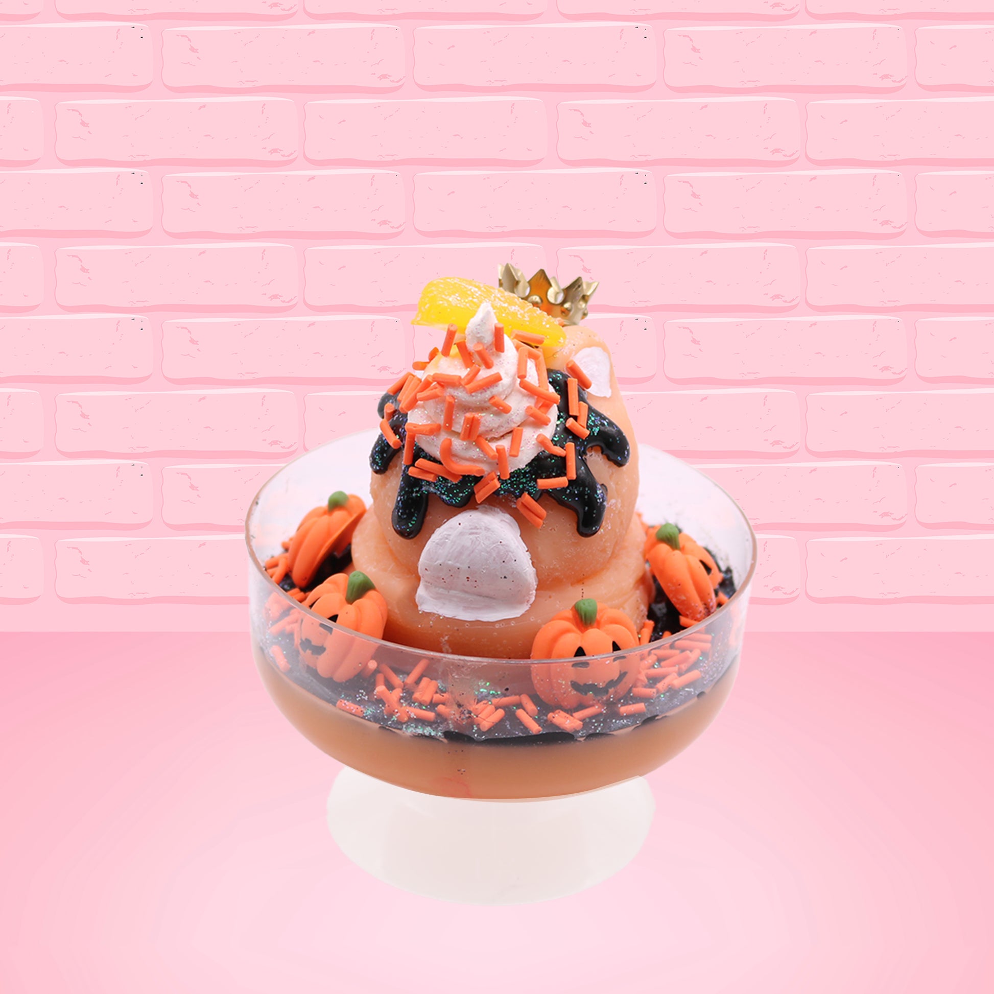 Cute kawaii Pumpkin King Bunny orange ice cream sundae with black glaze, orange sprinkles and pumpkin faces in the dish.  The bunny has a golden crown and orange slice on top next to the swirl of whipped cream. This view is from the back.