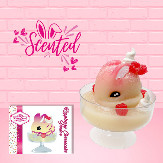 Cute kawaii bunny raspberry cheesecake white ice cream with raspberries and whipped cream swirls in the dish. The bunny has two raspberry on the back near the swirl of whipped cream and covered with white glitter. The character card front which has the digital artwork of the ice cream and the word scented is also shown.
