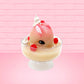 Cute kawaii bunny raspberry cheesecake white ice cream with raspberries and whipped cream swirls in the dish. The bunny has two raspberry on the back near the swirl of whipped cream and covered with white glitter. This view is from the front at an angle.