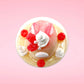 Cute kawaii bunny raspberry cheesecake white ice cream with raspberries and whipped cream swirls in the dish. The bunny has two raspberry on the back near the swirl of whipped cream and covered with white glitter. This view is from the top.