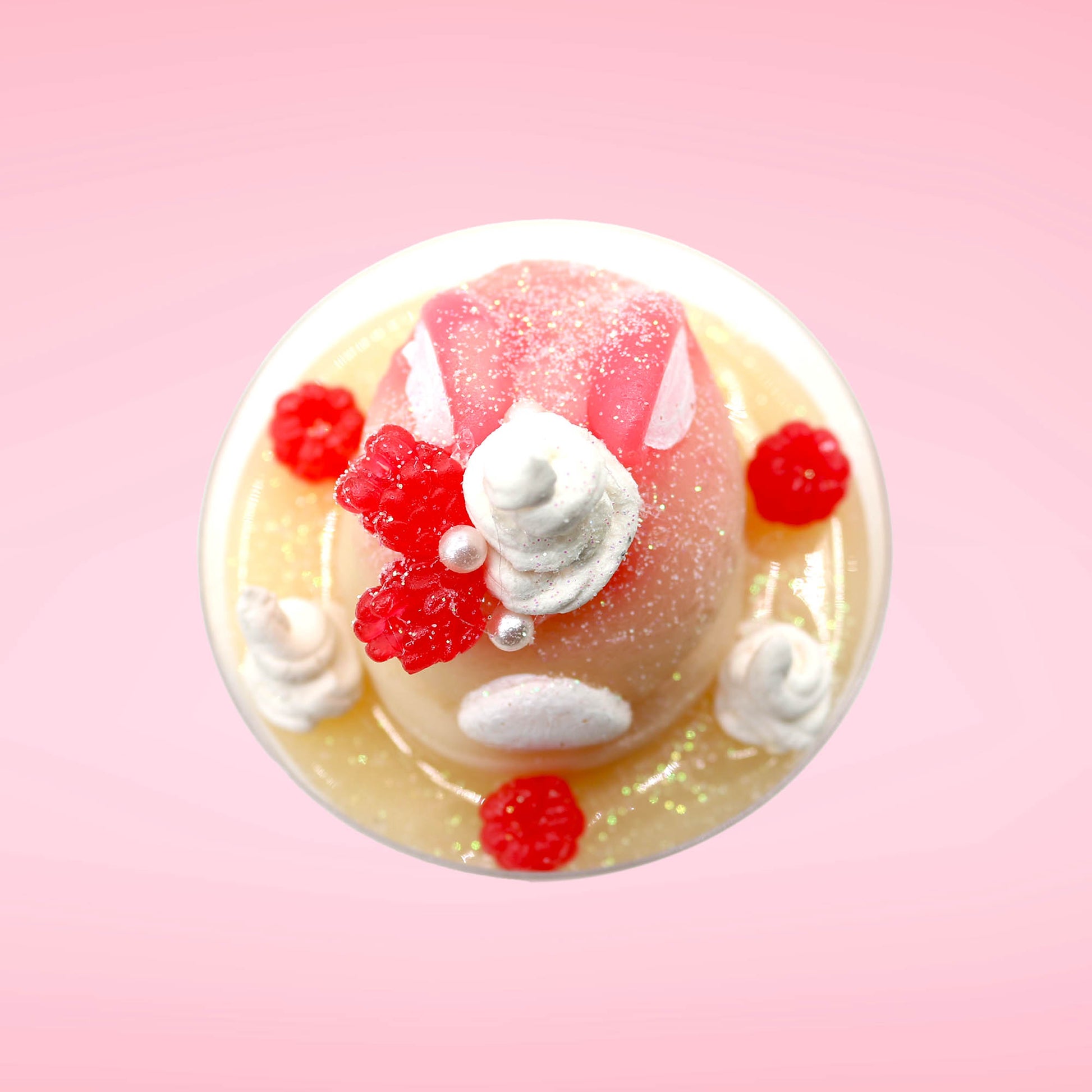 Cute kawaii bunny raspberry cheesecake white ice cream with raspberries and whipped cream swirls in the dish. The bunny has two raspberry on the back near the swirl of whipped cream and covered with white glitter. This view is from the top.
