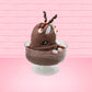 Cute kawaii bunny rocky on the rocks ice cream brown sundae with marshmallows and brown bits in the dish. The marshmallows on the top of the ice cream have red berries as well as two swirls of solid chocolate that stick up and a swirl of whipped cream is on the back. There are two chocolate balls and one red ball on between the ears of the ice cream bunny. This view is from the front at a slight angle.