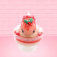Cute kawaii bunny Santa Cookie Crumble white ice cream sundae with red glaze, glitter, red berries and whipped swirls in the dish. The bunny has red berries and green leaves on top with red translucent glaze near the whipped cream swirl. This view is from the front.
