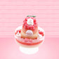 Cute kawaii bunny Santa Cookie Crumble white ice cream sundae with red glaze, glitter, red berries and whipped swirls in the dish. The bunny has red berries and green leaves on top with red translucent glaze near the whipped cream swirl. This view is from the back.