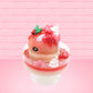 Cute kawaii bunny Santa Cookie Crumble white ice cream sundae with red glaze, glitter, red berries and whipped swirls in the dish. The bunny has red berries and green leaves on top with red translucent glaze near the whipped cream swirl. This view is from the other side.