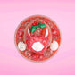 Cute kawaii bunny Santa Cookie Crumble white ice cream sundae with red glaze, glitter, red berries and whipped swirls in the dish. The bunny has red berries and green leaves on top with red translucent glaze near the whipped cream swirl. This view is from the top.