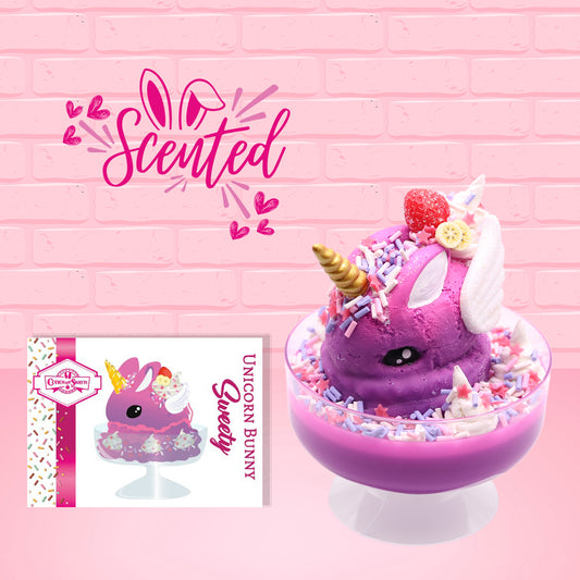 Cute kawaii unicorn purple and pink ice cream sundae with whipped cream swirls, purple, pink, white, and red star sprinkles in the dish. This unicorn bunny has white wings with a strawberry, banana slices and sprinkles on top near the whipped cream. The front of the character card and word scented is shown. 