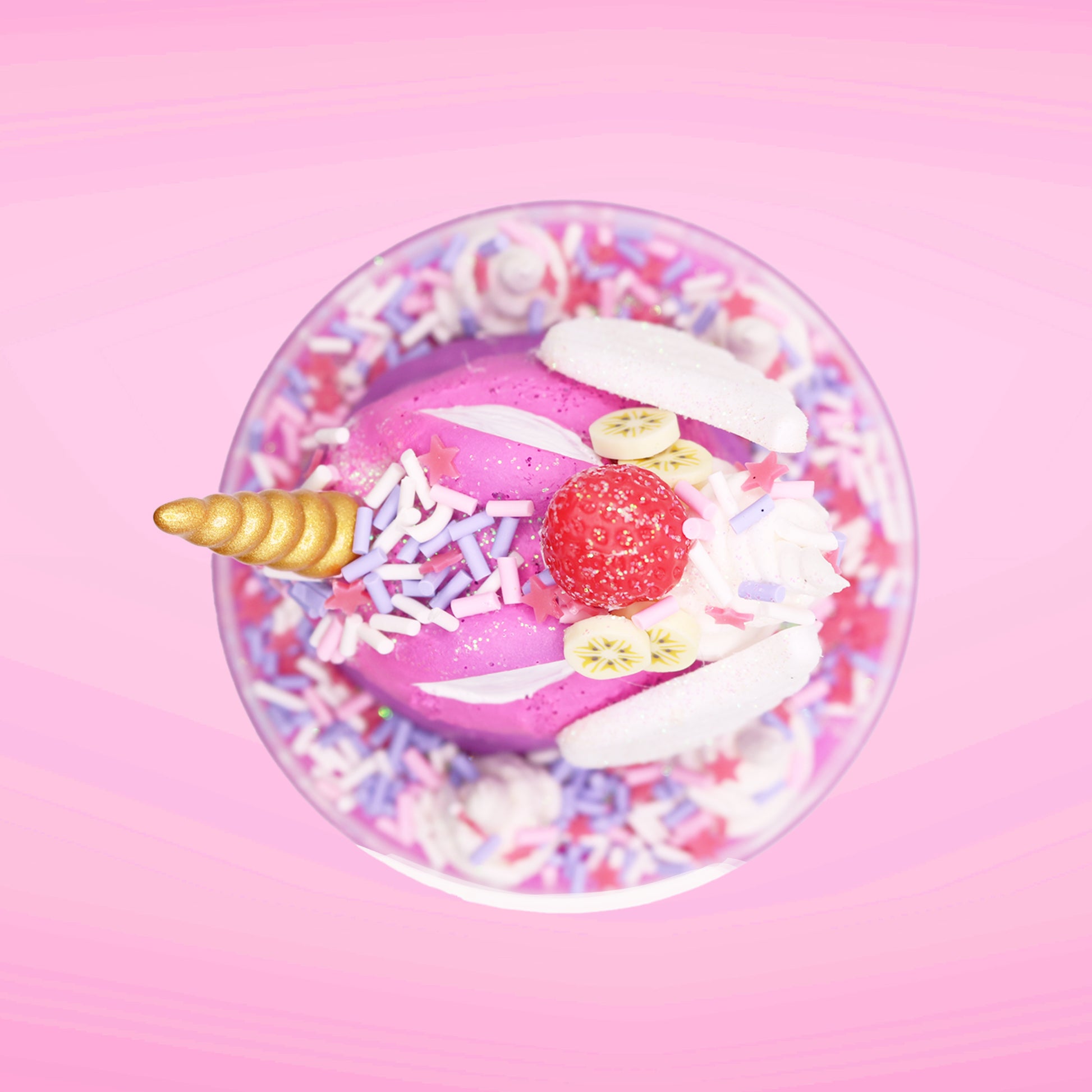 Cute kawaii unicorn purple and pink ice cream sundae with whipped cream swirls, purple, pink, white, and red star sprinkles in the dish. This unicorn bunny has white wings with a strawberry, banana slices and sprinkles on top near the whipped cream. This view is from the top. 