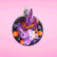 Cute kawaii witch bunny Blair purple ice cream with purple crystals and pumpkins on top of a layer of glittery black translucent layer. The bunny has a purple witch’s hat, with purple raspberries and a whipped cream swirl on top, with black glittery glaze and orange sprinkles. This view is from the top.