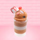 Cute kawaii bunny Gingerbread Mousse tall ice cream sundae that has white crumbles, a gingerbread man with a santa hat, and a marshmallow with glittery red glaze in the dish.  The bunny has peppermint candies, a strawberry, and a swirl of whipped cream on top and a snowflake on the front. This view is from the side.