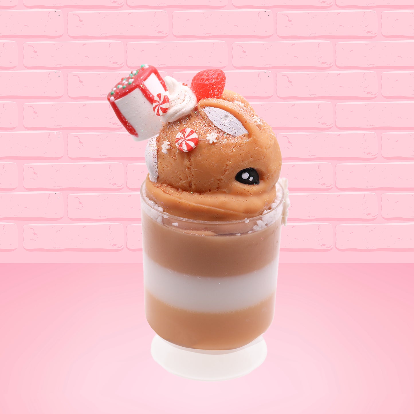 Cute kawaii bunny Gingerbread Mousse tall ice cream sundae that has white crumbles, a gingerbread man with a santa hat, and a marshmallow with glittery red glaze in the dish.  The bunny has peppermint candies, a strawberry, and a swirl of whipped cream on top and a snowflake on the front. This view is from the side.