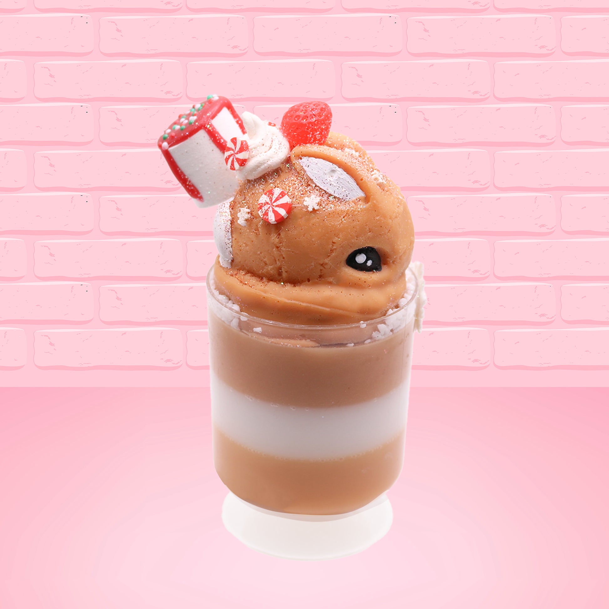 Cute kawaii bunny Gingerbread Mousse tall ice cream sundae that has white crumbles, a gingerbread man with a santa hat, and a marshmallow with glittery red glaze in the dish.  The bunny has peppermint candies, a strawberry, and a swirl of whipped cream on top and a snowflake on the front. This view is from the side.