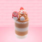 Cute kawaii bunny Gingerbread Mousse tall ice cream sundae that has white crumbles, a gingerbread man with a santa hat, and a marshmallow with glittery red glaze in the dish.  The bunny has peppermint candies, a strawberry, and a swirl of whipped cream on top and a snowflake on the front. This view is from the back.
