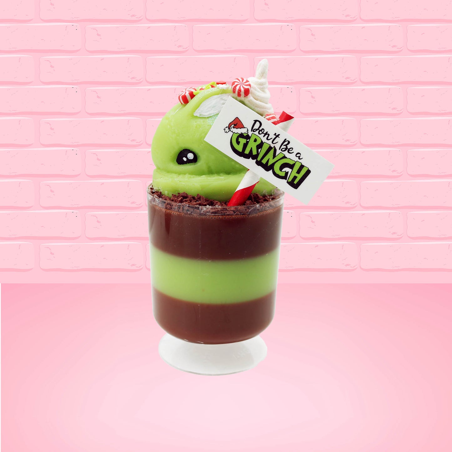 Cute kawaii bunny green Grinch Brownie tall sundae with brown sprinkles in the cup as well as a sign that reads don’t be a grinch. The ice cream bunny has peppermint candies, green and white sprinkles as well as a swirl of whipped cream on top. This view is from the side. 