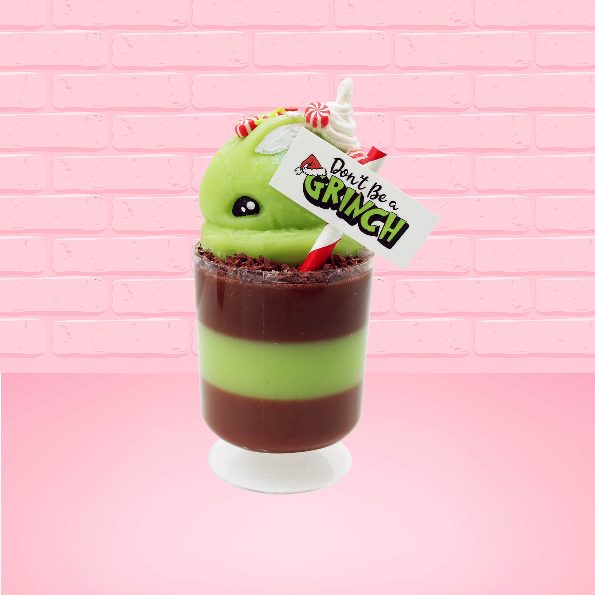 Cute kawaii bunny green Grinch Brownie tall sundae with brown sprinkles in the cup as well as a sign that reads don’t be a grinch. The ice cream bunny has peppermint candies, green and white sprinkles as well as a swirl of whipped cream on top. This view is from the side. 