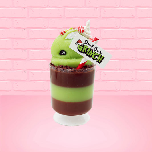 Cute kawaii bunny green Grinch Brownie tall sundae with brown sprinkles in the cup as well as a sign that reads don’t be a grinch. The ice cream bunny has peppermint candies, green and white sprinkles as well as a swirl of whipped cream on top. This view is from the side. 