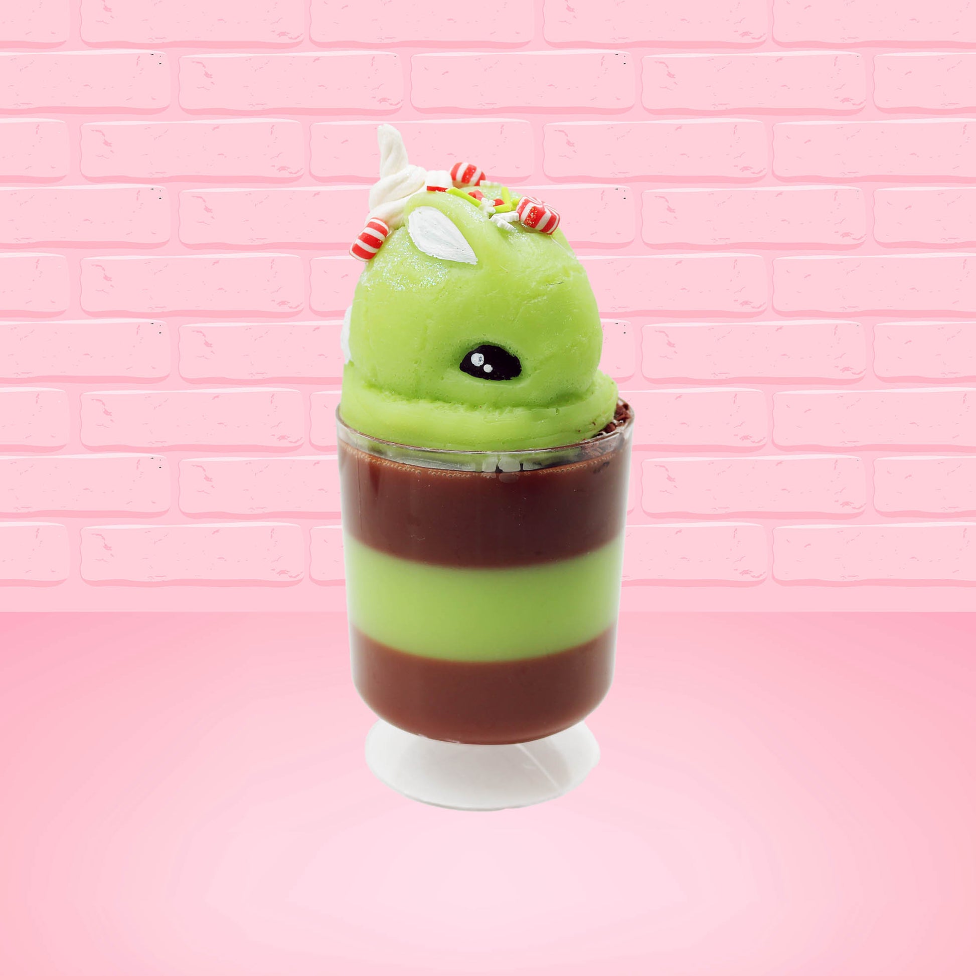 Cute kawaii bunny green Grinch Brownie tall sundae with brown sprinkles in the cup as well as a sign that reads don’t be a grinch.  The ice cream bunny has peppermint candies, green and white sprinkles as well as a swirl of whipped cream on top.  This view is from the front at an angle.