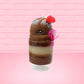 Cute kawaii bunny tall brown Hot Fudge ice cream sundae with glitter and raspberries on top with the whipped cream swirl. The bunny has white pearls and a pink ribbon. This view is from the side.