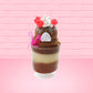 Cute kawaii bunny tall brown Hot Fudge ice cream sundae with glitter and raspberries on top with the whipped cream swirl. The bunny has white pearls and a pink ribbon. This view is from the back.