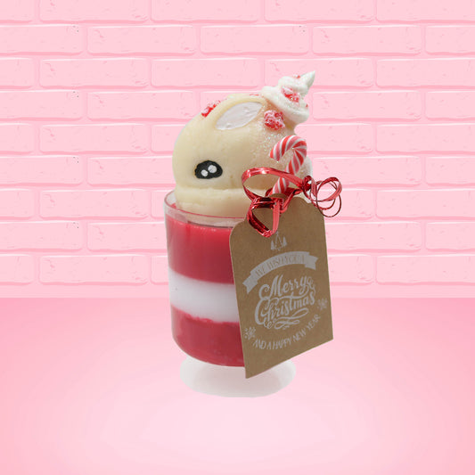Cute kawaii bunny Peppermint Bark white ice cream tall sundae that has red and white layers in the dish and a peppermint candy cane holding a brown and white tag. The tag reads We wish you a merry Christmas and a happy new year, and the bunny has bits of peppermint candy on top as well as swirl of whipped cream. This view is from the side.