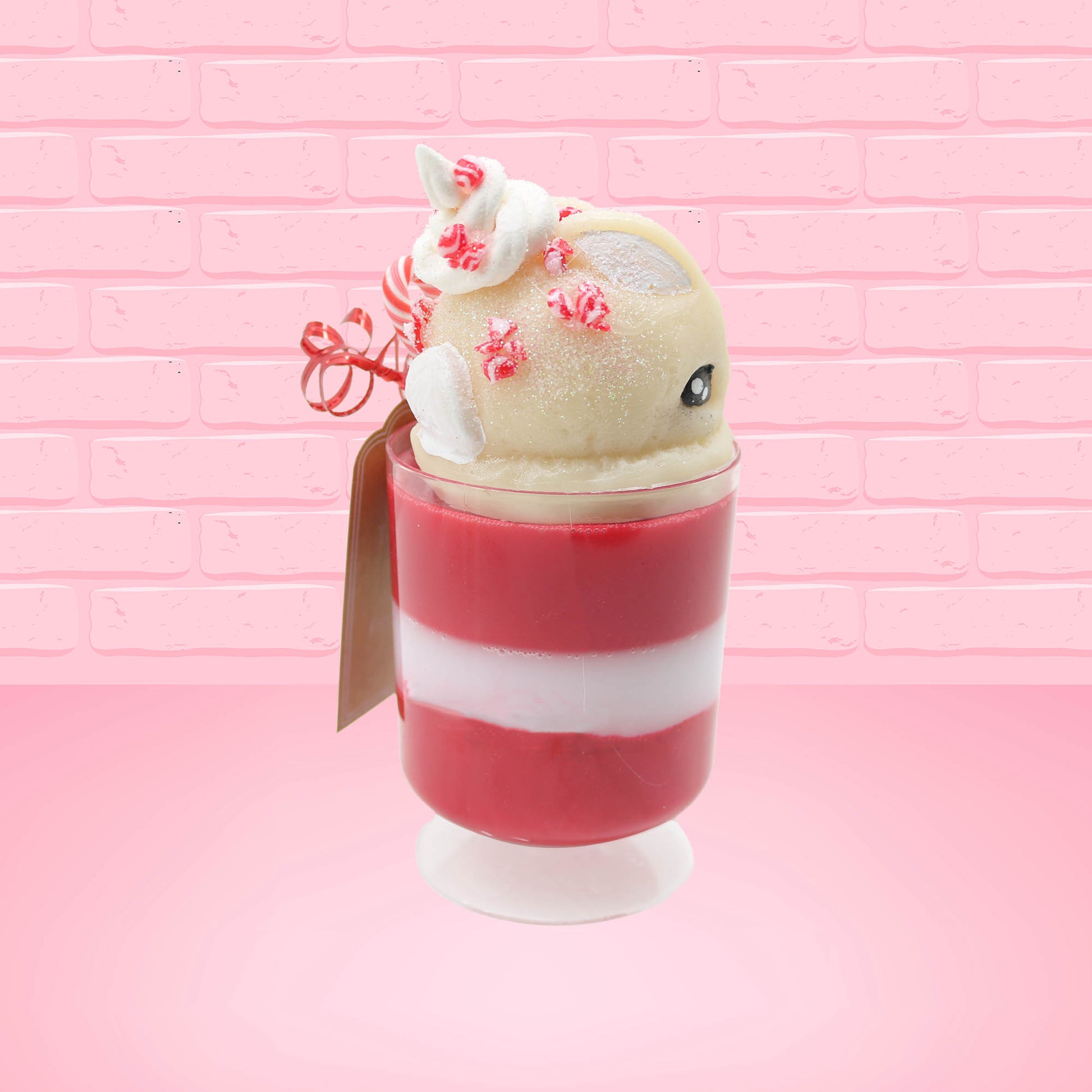 Cute kawaii bunny Peppermint Bark white ice cream tall sundae that has red and white layers in the dish and a peppermint candy cane holding a brown and white tag. The tag reads We wish you a merry Christmas and a happy new year, and the bunny has bits of peppermint candy on top as well as swirl of whipped cream. This view is from the other side.