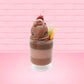 Cute kawaii bunny tall brown and light brown ice cream sundae with brown chocolate crumbles over the bunny, with a cherry on top of the whipped cream swirl.  Three bendy gummy worms are in the dish on the side. This view is from the front.