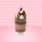 Cute kawaii bunny tall brown and light brown ice cream sundae with brown chocolate crumbles over the bunny, with a cherry on top of the whipped cream swirl.  Three bendy gummy worms are in the dish on the side. This view is from the back.